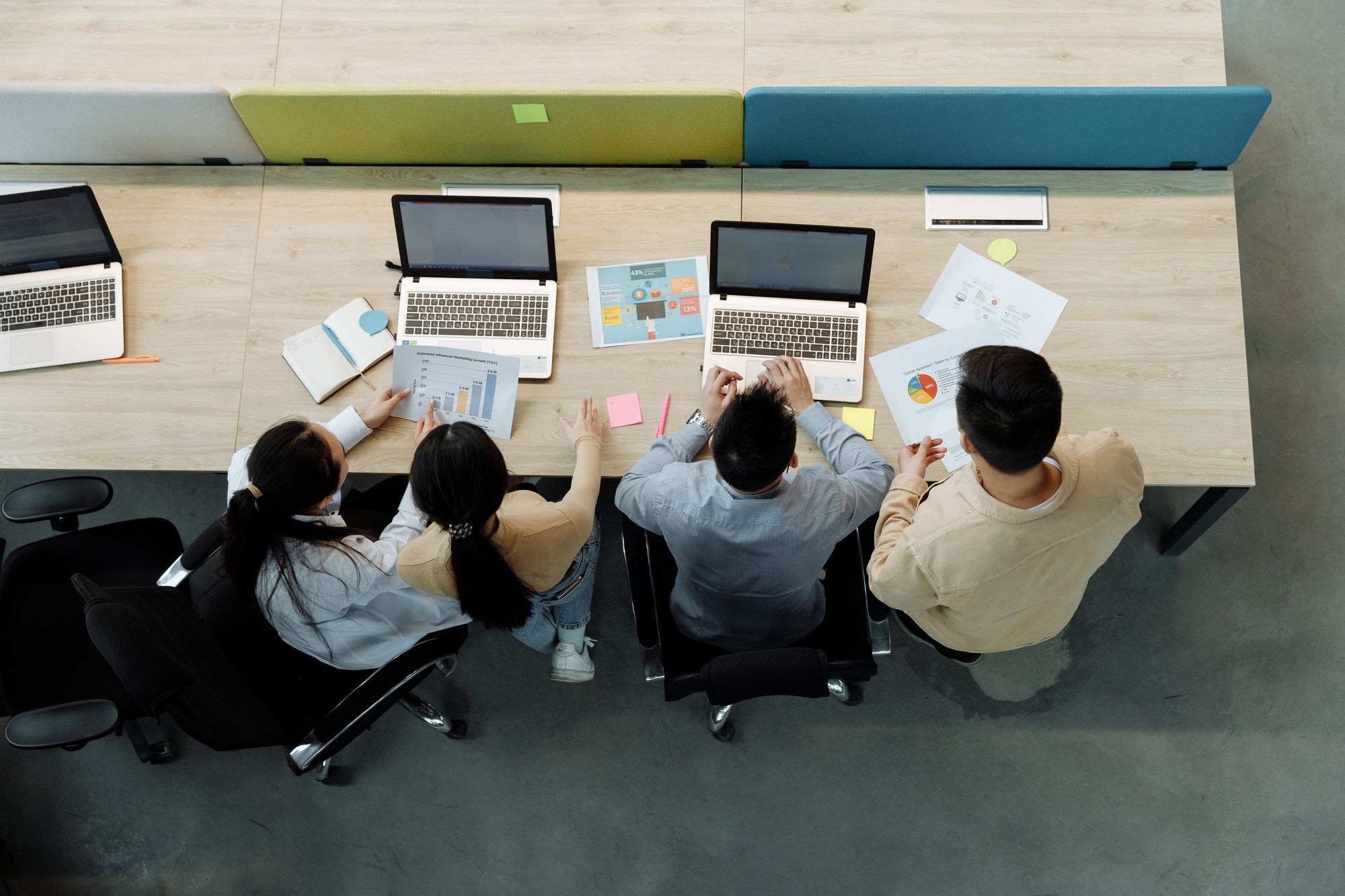 Vista de cima de quatro pessoas trabalhando em notebooks numa mesa compartilhada de escritório